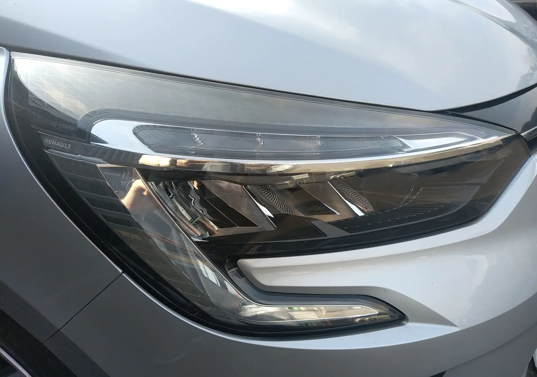 Gros plan sur le phare avant droit gris d'une Renault Clio V 2023, mettant en valeur ses lignes LED modernes.