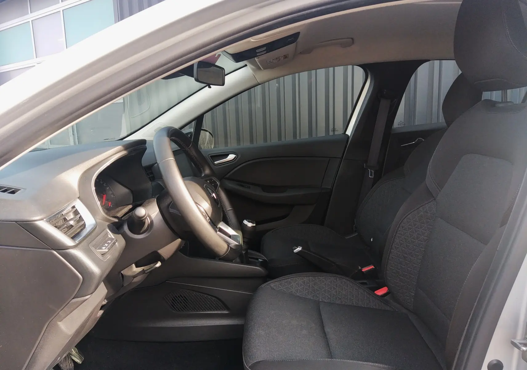 Vue intérieure côté conducteur de la Renault Clio V 2023, sièges tissu noir et volant multifonction.