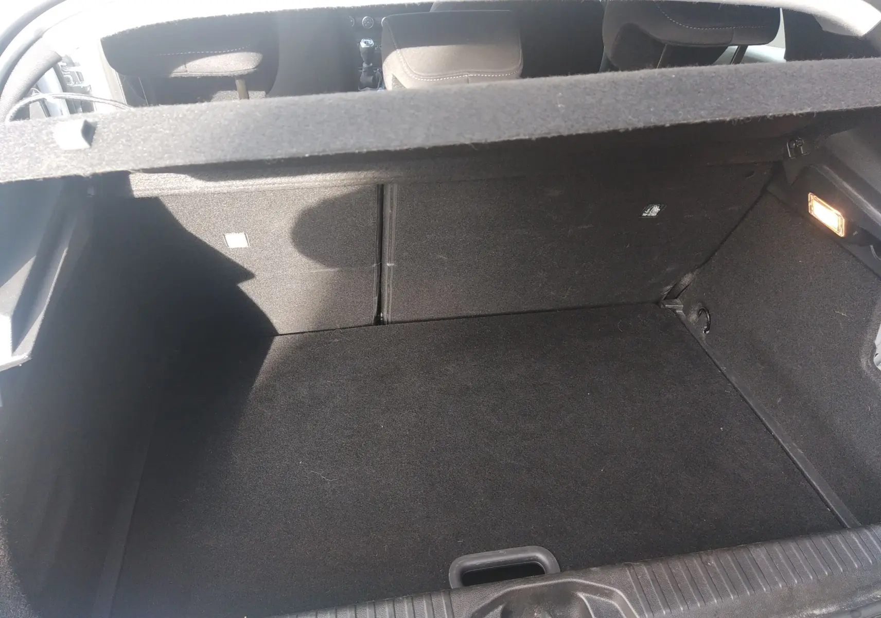 Vue intérieure du coffre spacieux et propre de la Renault Clio V gris, avec banquette arrière visible en arrière-plan.