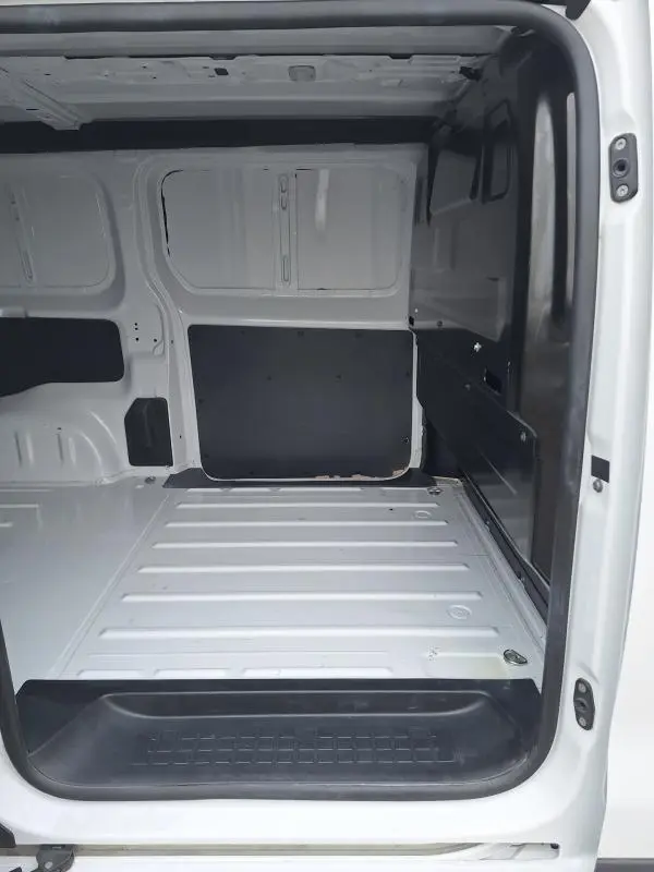 Intérieur du fourgon Opel Vivaro blanc vu de l'ouverture latérale, montrant l'espace de chargement vide et les parois métalliques.