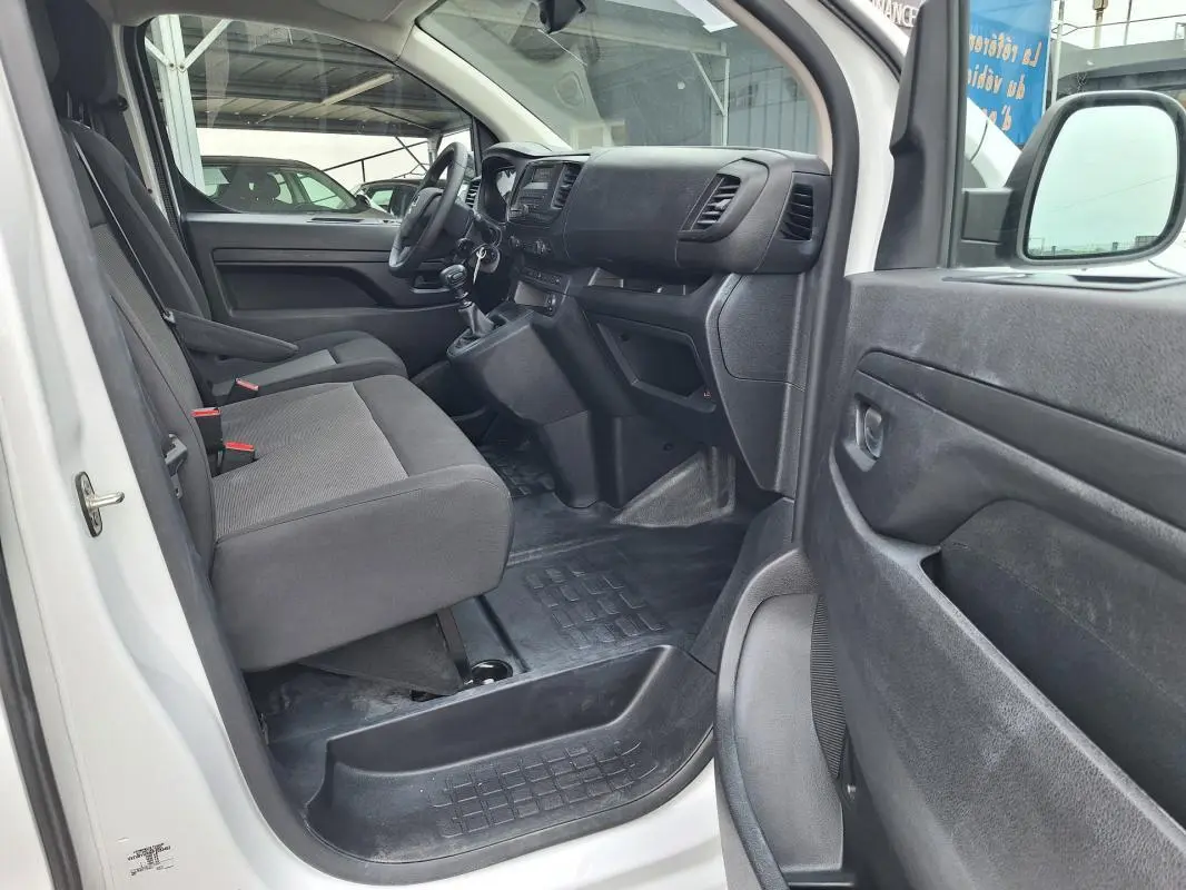 Vue intérieure côté conducteur de l'Opel Vivaro blanc 2025, montrant les sièges avant et le tableau de bord noir.