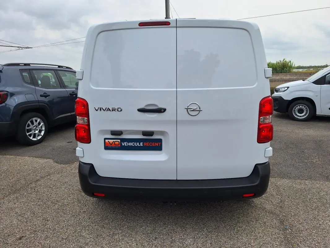 Vue arrière d’un fourgon Opel Vivaro blanc, avec portes battantes fermées et feux rouges visibles.