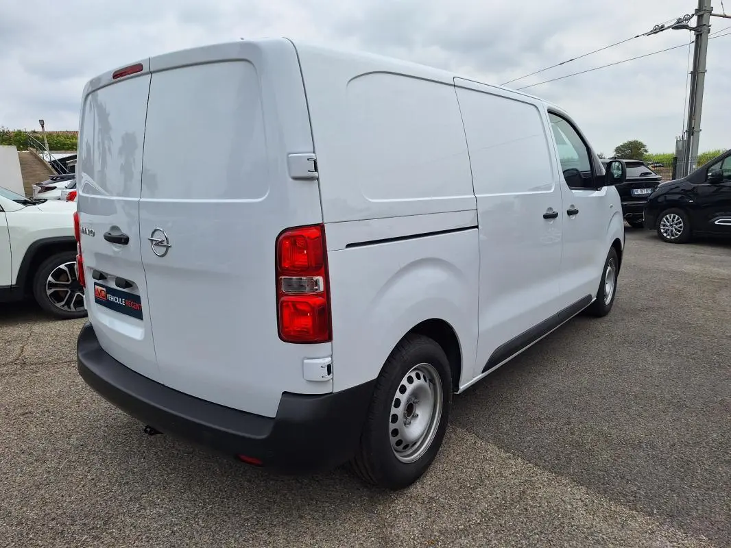 Opel Vivaro blanc vu en 3/4 arrière droit, fourgon utilitaire avec porte latérale et feux arrière rouges.