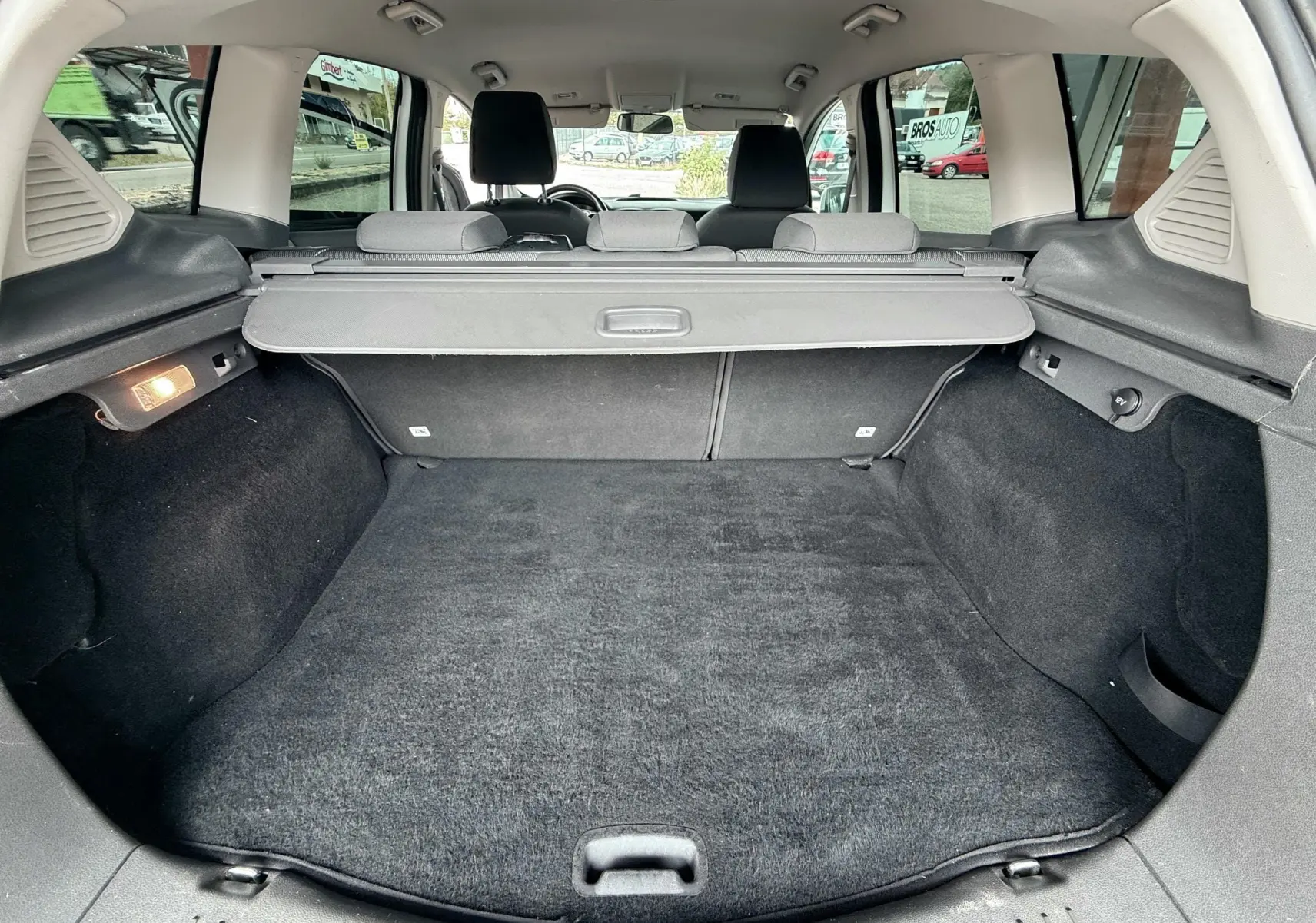 Coffre spacieux du Ford Kuga blanc vu de l'arrière avec cache-bagages et intérieur en tissu gris noir.