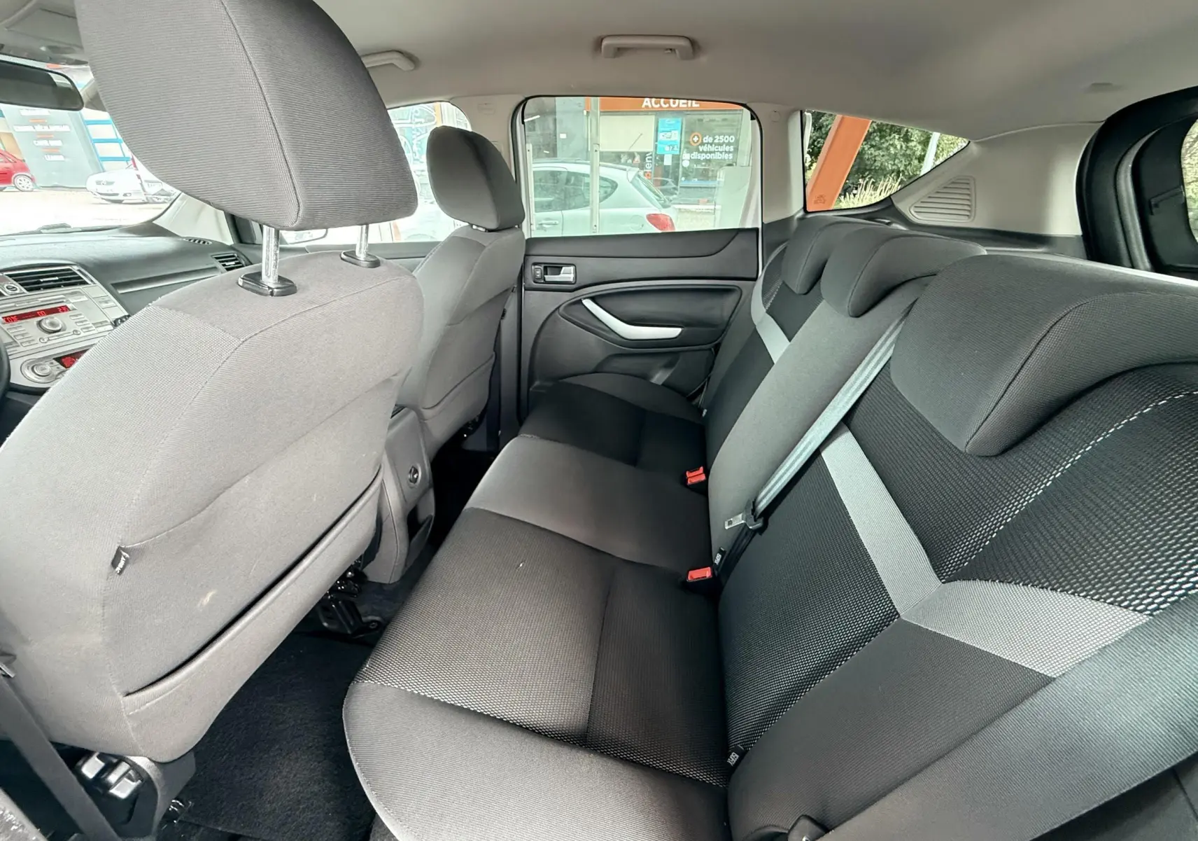 Vue intérieure arrière du Ford Kuga 2012 montrant la banquette en tissu gris noir et les ceintures de sécurité grises.
