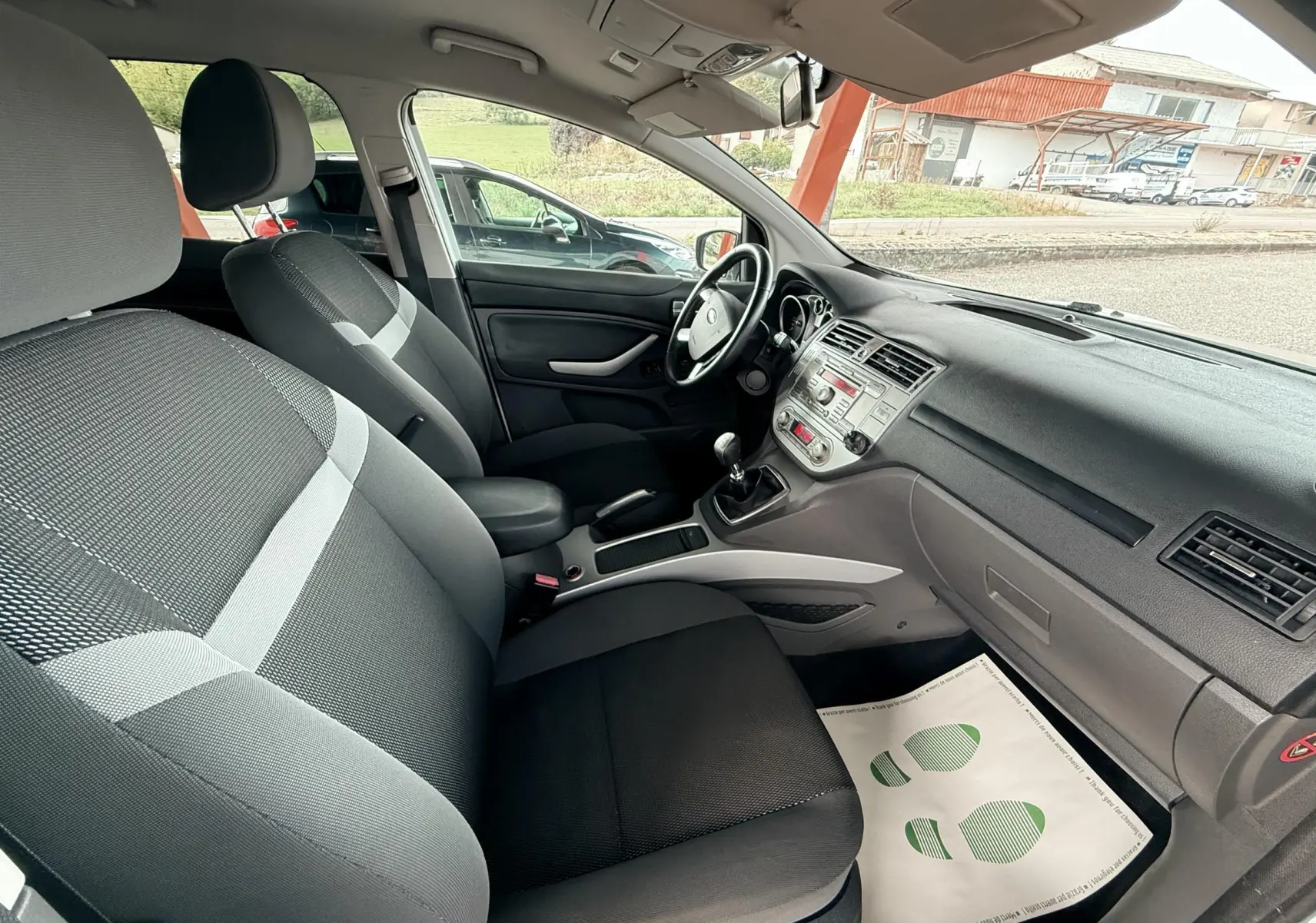 Intérieur avant droit du Ford Kuga 2012 avec sièges tissu gris et tableau de bord noir simple et fonctionnel.