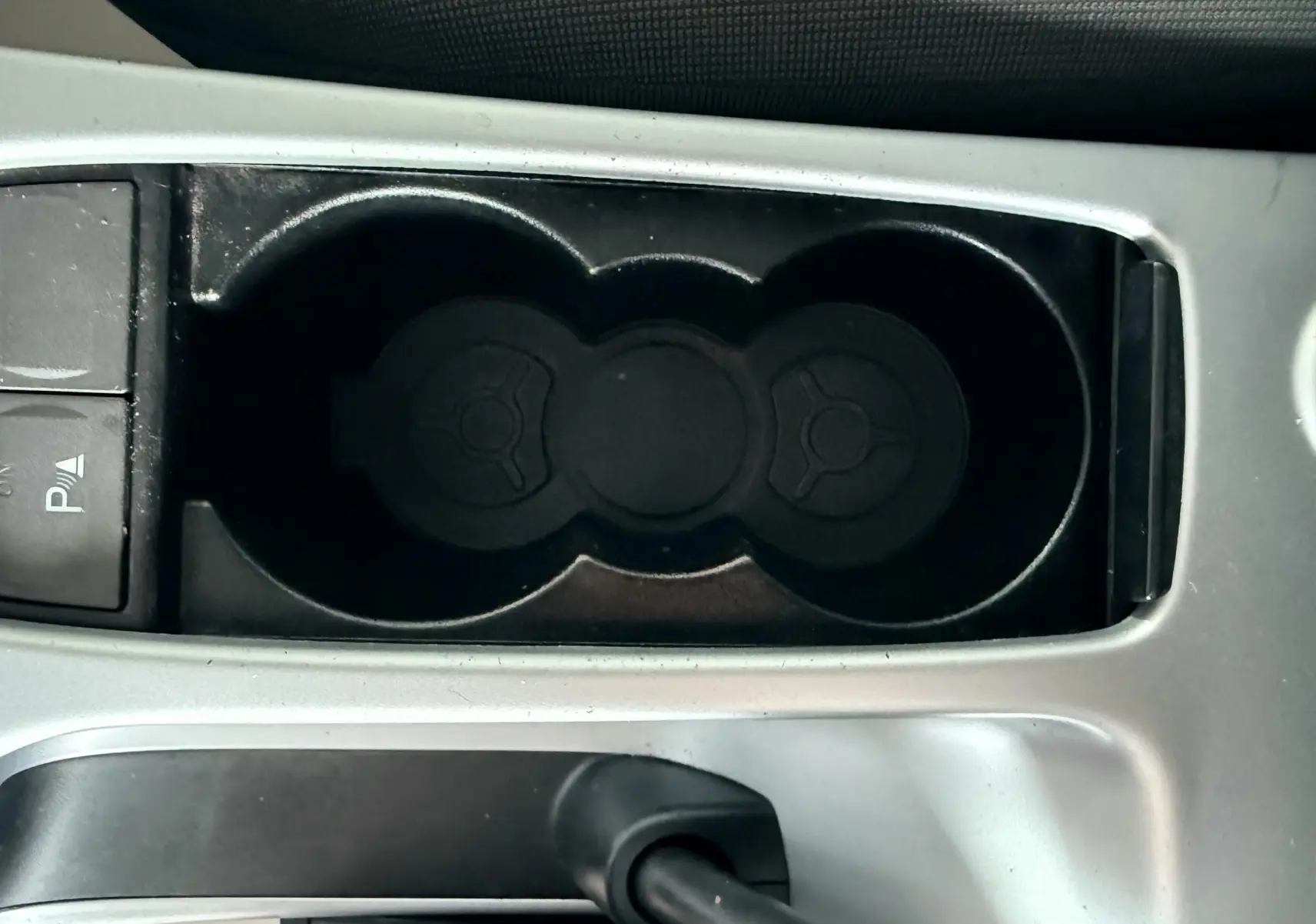 Gros plan sur le porte-gobelets et le frein à main noir dans l'habitacle gris d'une Ford Kuga 2012.