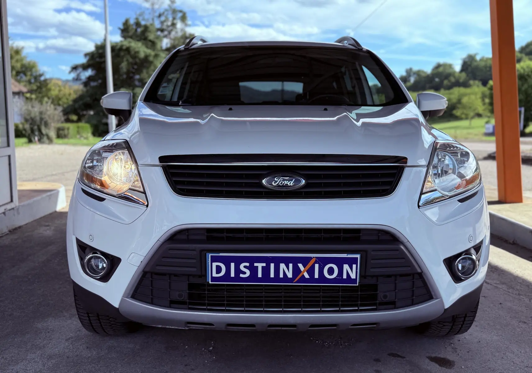 Vue frontale d'un Ford Kuga blanc de 2012 avec phares allumés et plaque Distinxion visible.