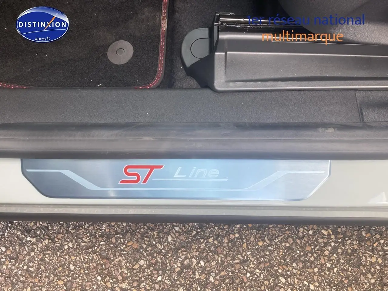 Gros plan sur la plaque de seuil de porte ST Line d'une Ford Puma gris cactus avec tapis noir et surpiqûres rouges visible.