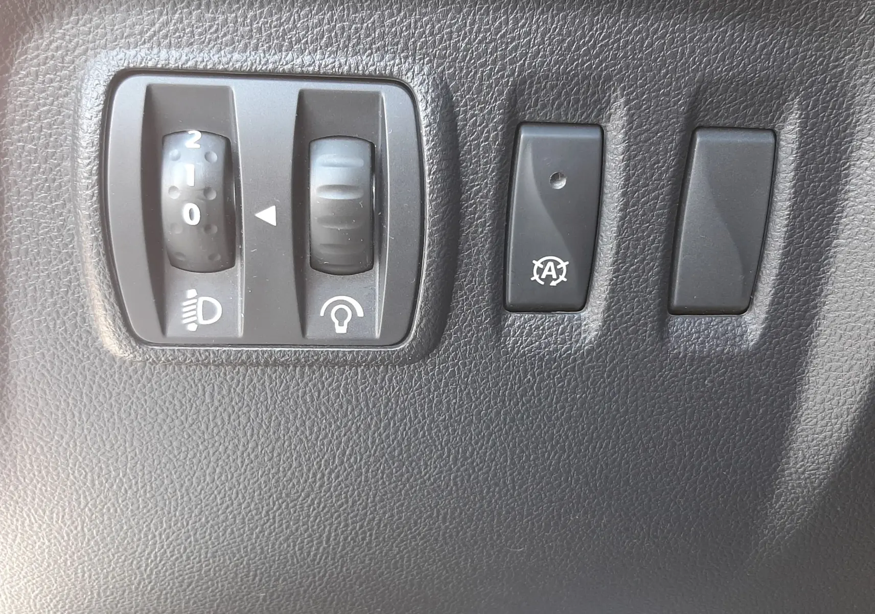 Gros plan sur les commandes de réglage des phares et bouton d'arrêt automatique du moteur du Renault Captur blanc nacré 2019.