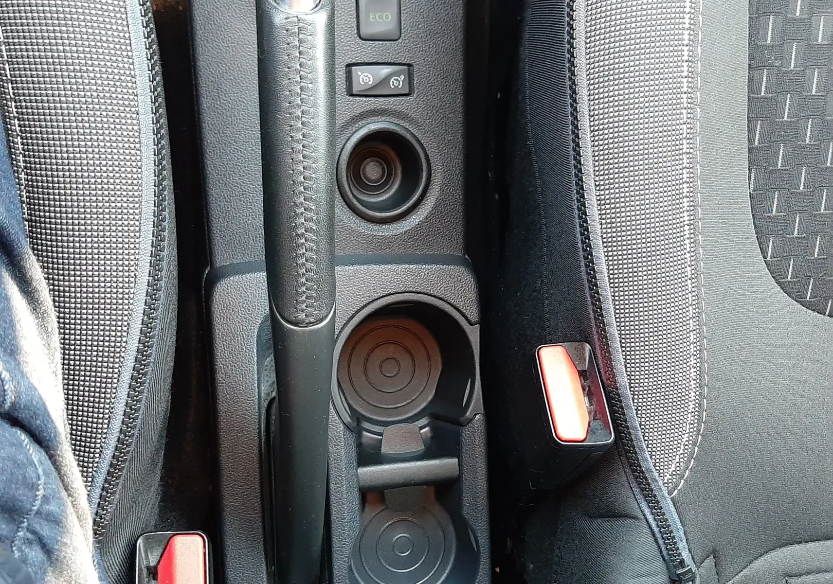 Vue plongeante sur la console centrale du Renault Captur blanc nacré, montrant frein à main, porte-gobelets et sièges tissu gris-noir.