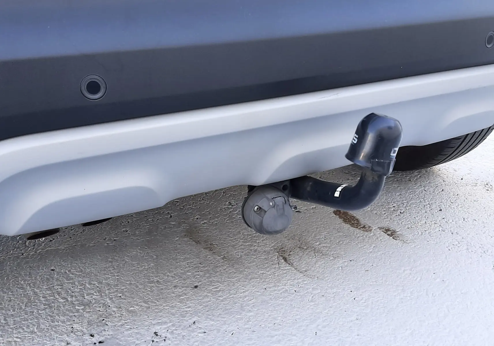 Gros plan sur l'attelage de remorque sous le pare-chocs arrière gris d'un Renault Captur blanc nacré avec toit noir.