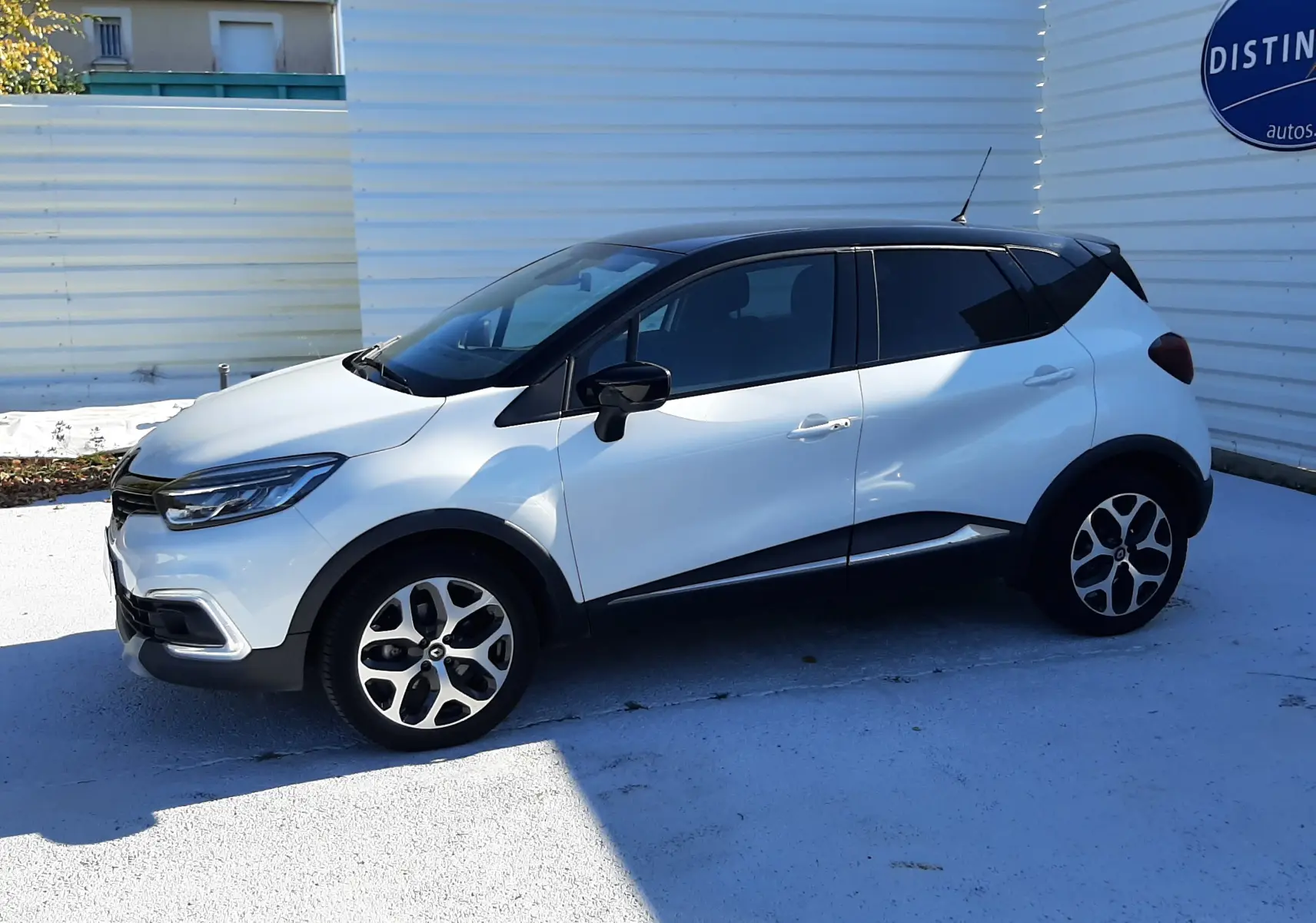 Renault Captur blanc nacré avec toit noir vu de profil côté gauche, soulignant ses jantes alliage et lignes modernes.