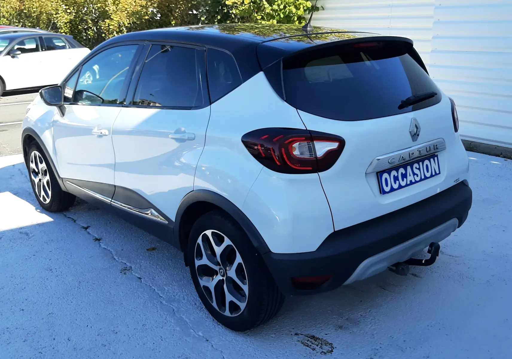 Renault Captur blanc nacré avec toit noir vu en 3/4 arrière droit, équipé de jantes alliage et attelage.