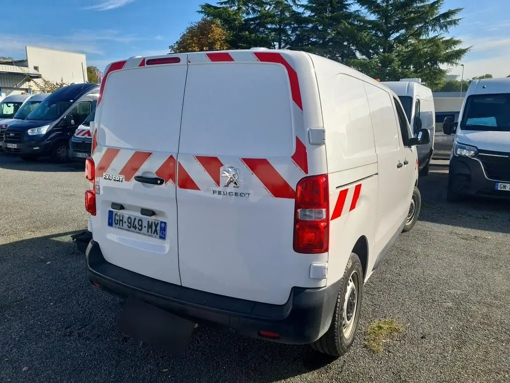 Vue 3/4 arrière d'un Peugeot Expert Fourgon blanc 2022 avec bandes réfléchissantes rouges et gyrophare.