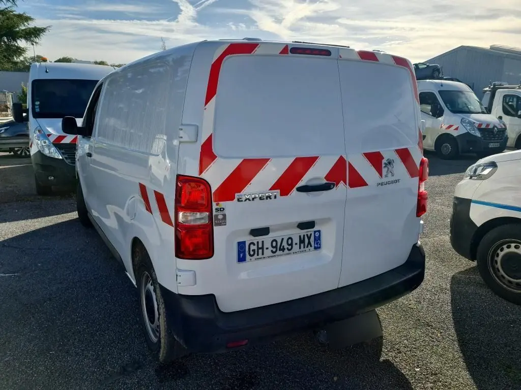 Vue arrière droite d'un Peugeot Expert Fourgon blanc 2022 avec bandes rouges réfléchissantes et gyrophare au toit.