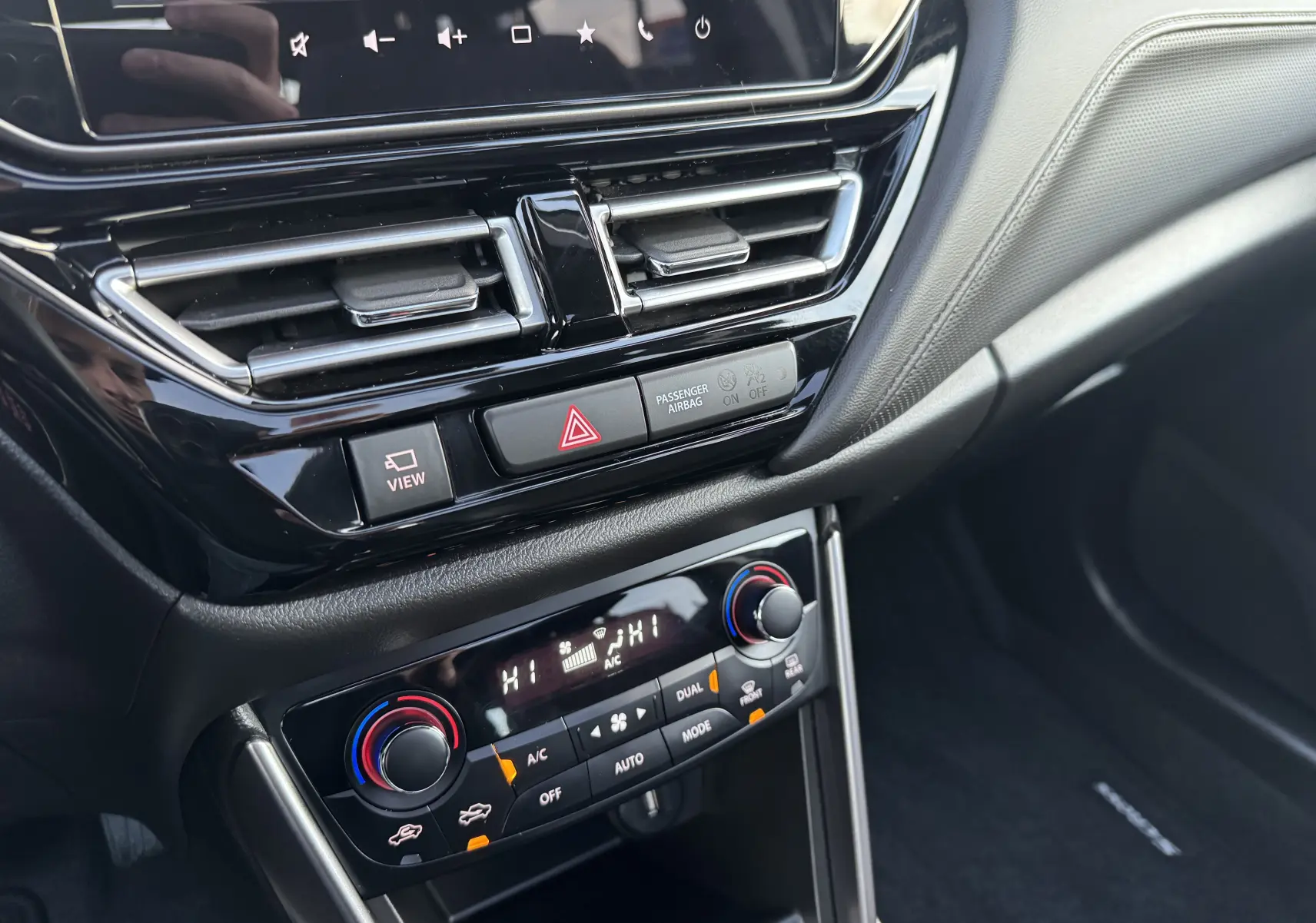 Gros plan sur la console centrale du Suzuki S-Cross blanc 2023, montrant les commandes de climatisation et les aérateurs.