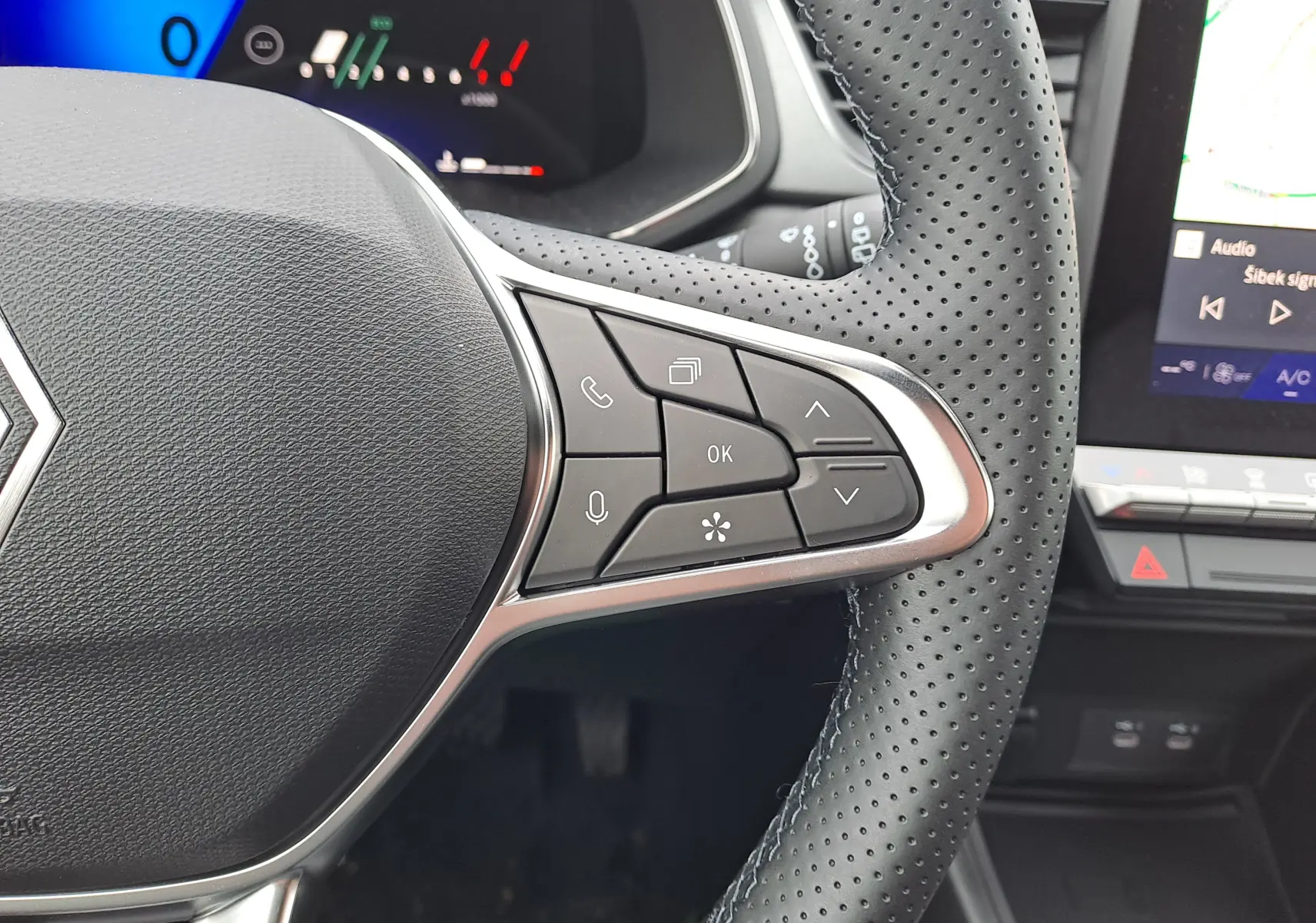 Vue rapprochée du volant perforé noir de la Renault Symbioz avec commandes multifonctions et tableau de bord digital partiel.