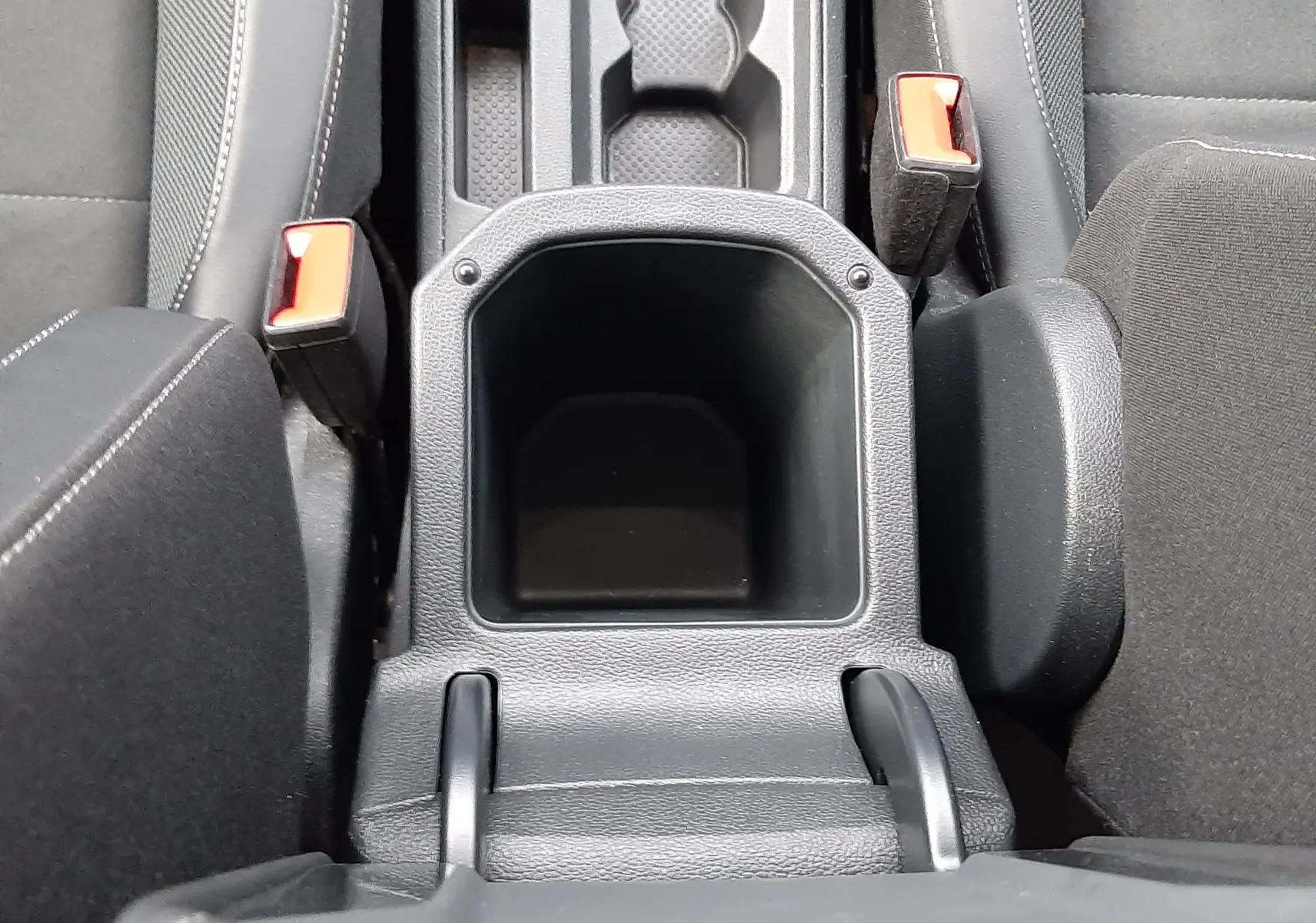 Vue plongeante sur la console centrale noire du Volkswagen T-Roc 2023, avec porte-gobelets et ceintures rouges visibles.