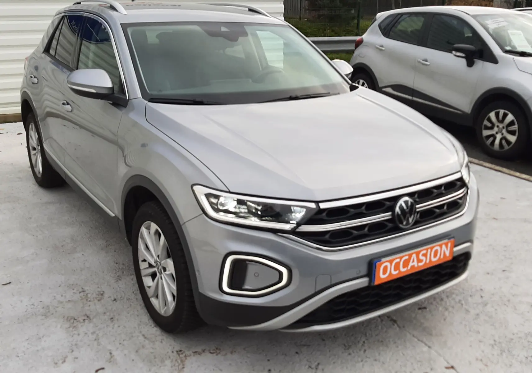 Volkswagen T-Roc gris pyrite vu en 3/4 avant droit avec calandre distinctive et plaques "OCCASION" visible.