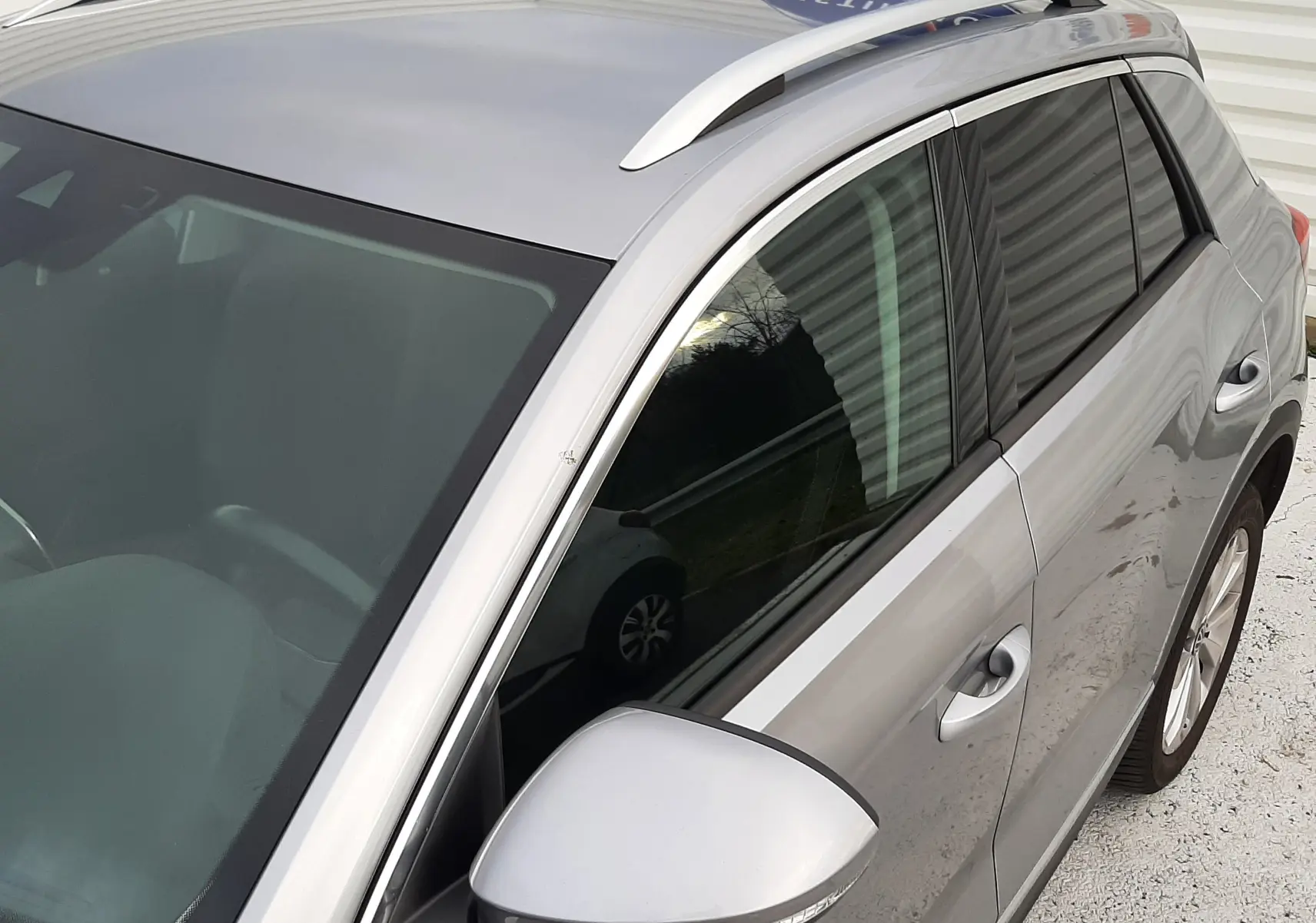 Vue en plongée du côté gauche d'un Volkswagen T-Roc gris pyrite avec vitres arrière surteintées et barres de toit argentées.