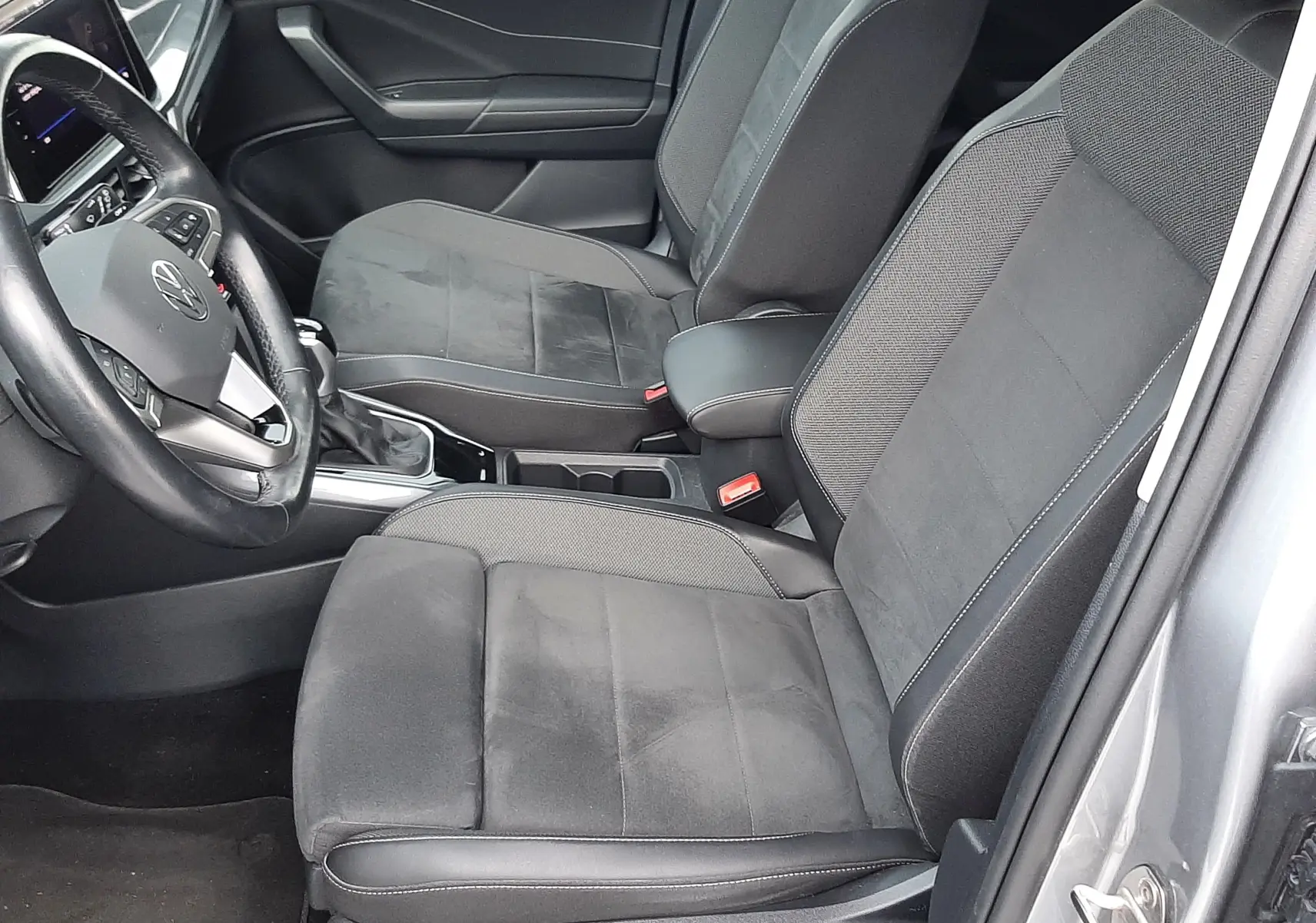 Vue intérieure côté conducteur du Volkswagen T-Roc gris pyrite, montrant les sièges noirs en tissu et alcantara avec console centrale.