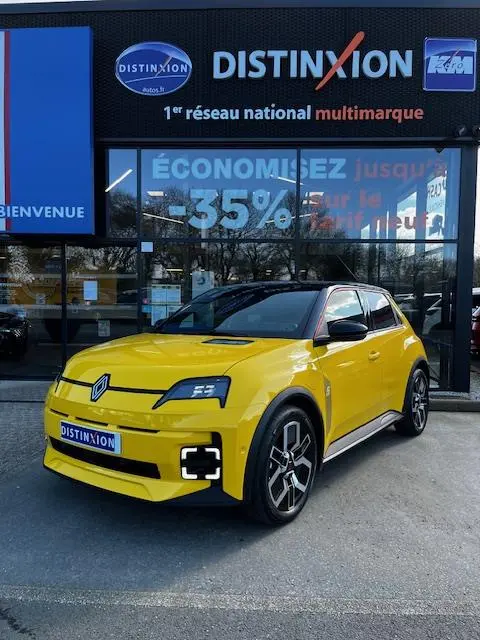 Renault R5 Techno jaune vue 3/4 avant droite, avec phares LED et jantes noires distinctives, devant un showroom Distinxion.