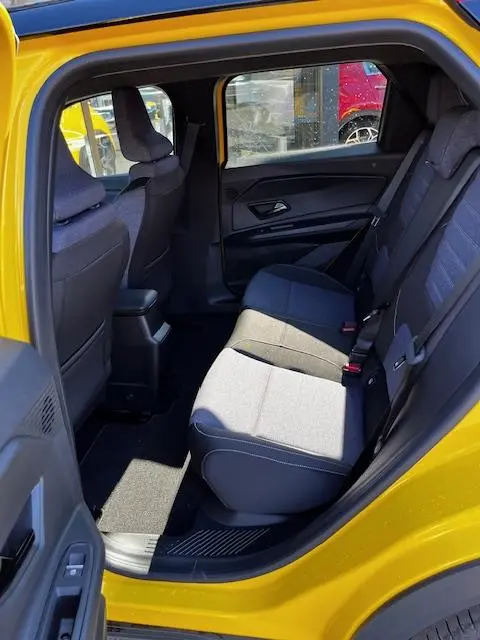 Vue intérieure arrière côté gauche de la Renault R5 Techno jaune 2024, montrant les sièges arrière en tissu gris et noir.