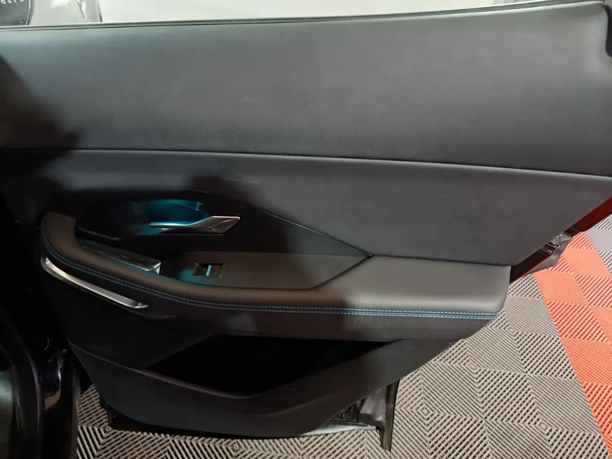 Gros plan sur la porte intérieure côté gauche du Jaguar E-PACE noir, avec surpiqûres bleues et poignée métal.