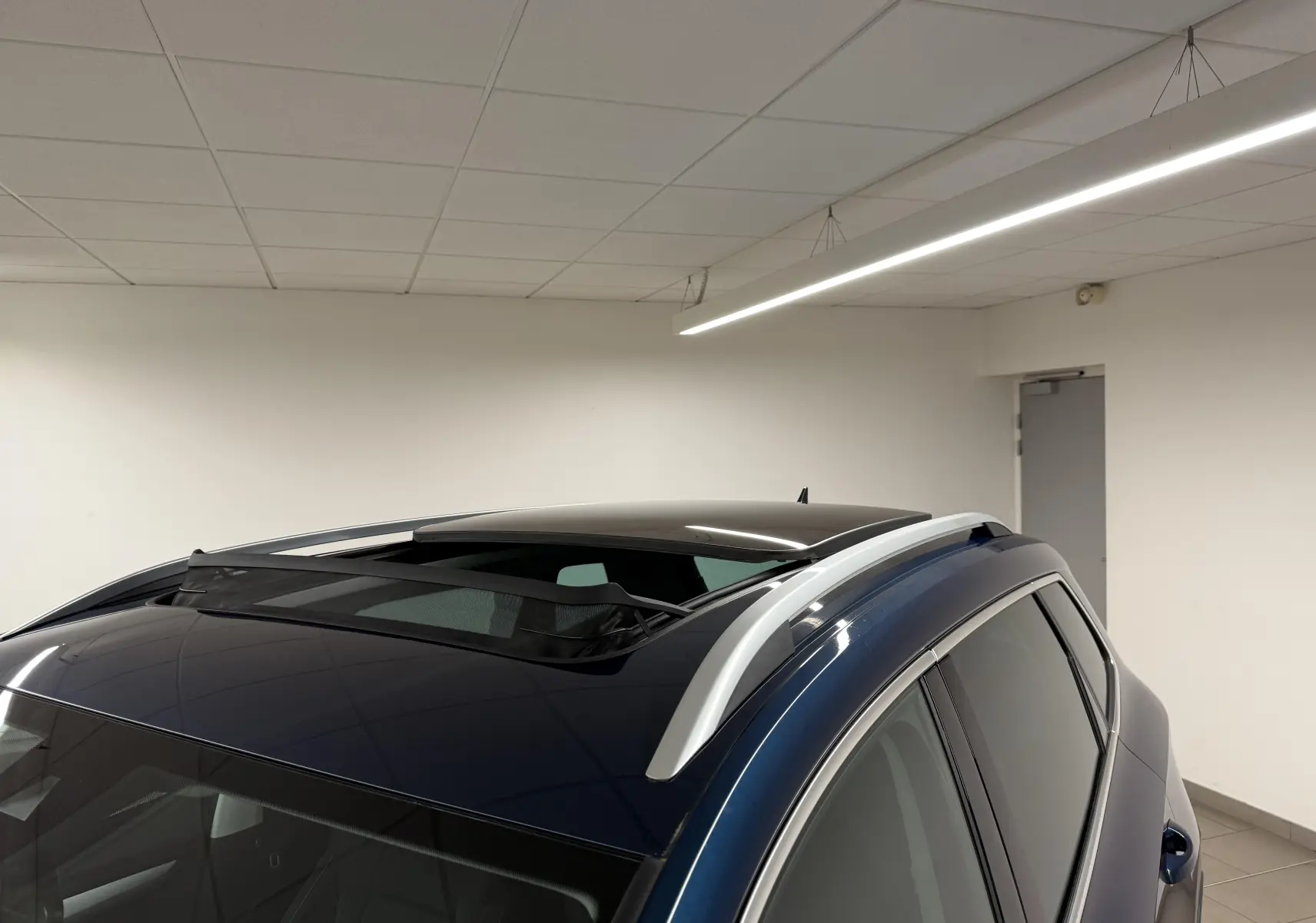Vue de dessus arrière droite du Skoda Karoq bleu lave avec toit ouvrant et barres de toit argentées.