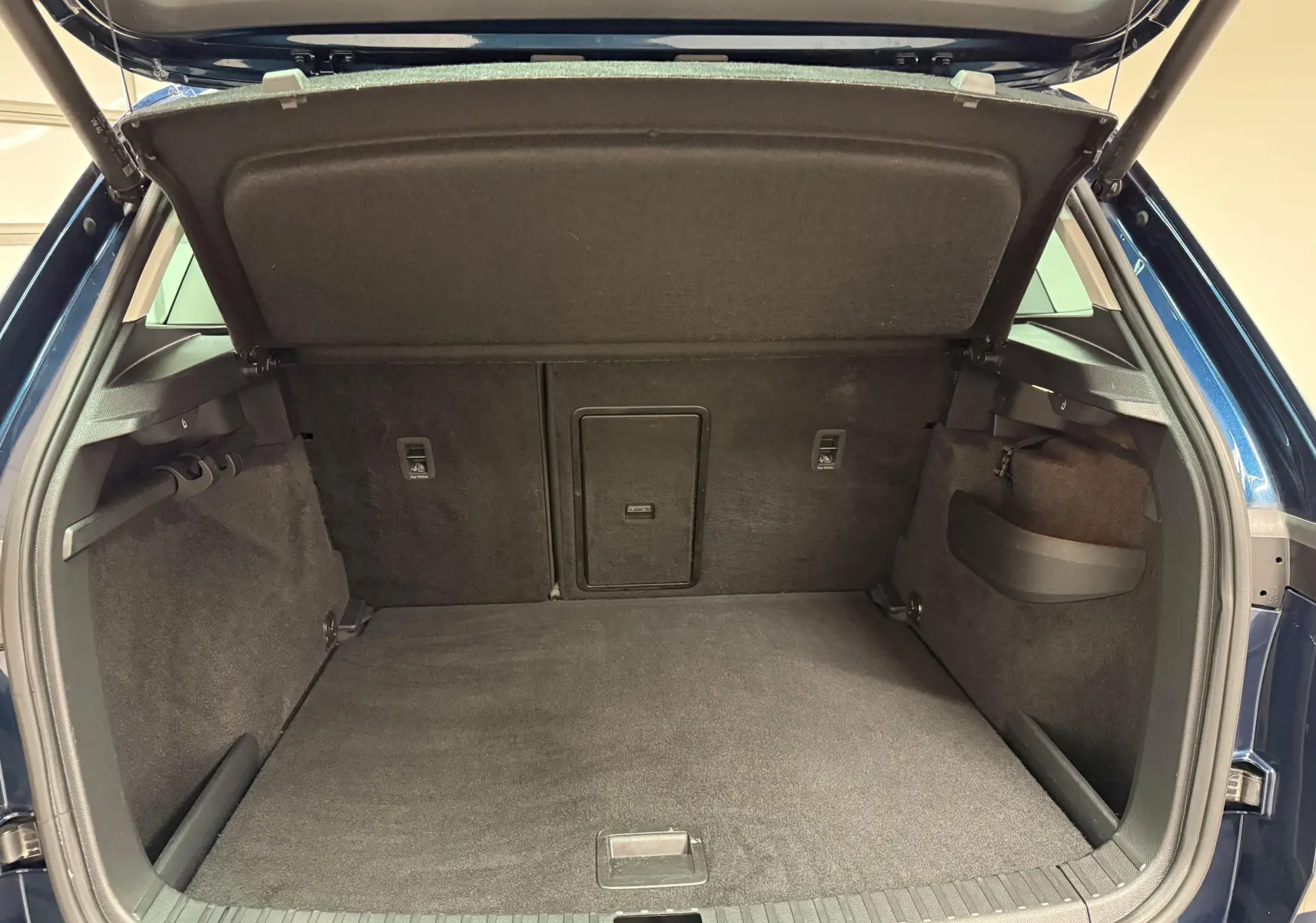 Coffre ouvert vu de l'arrière d'un Skoda Karoq bleu lave 2023, espace de chargement vide et tapis noir.
