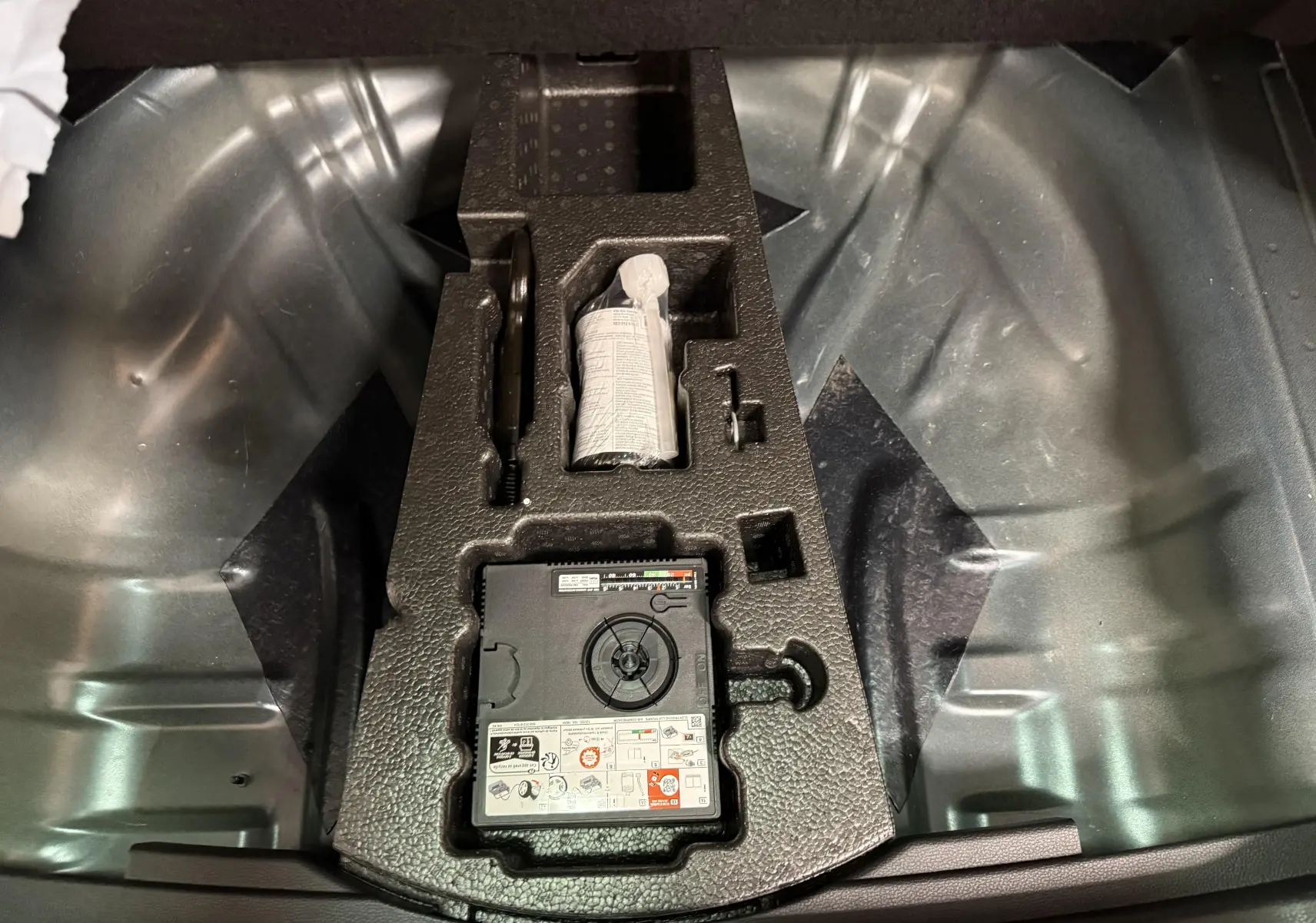 Gros plan sur la roue de secours galette et le kit de réparation dans le coffre d’un Skoda Karoq 2023.