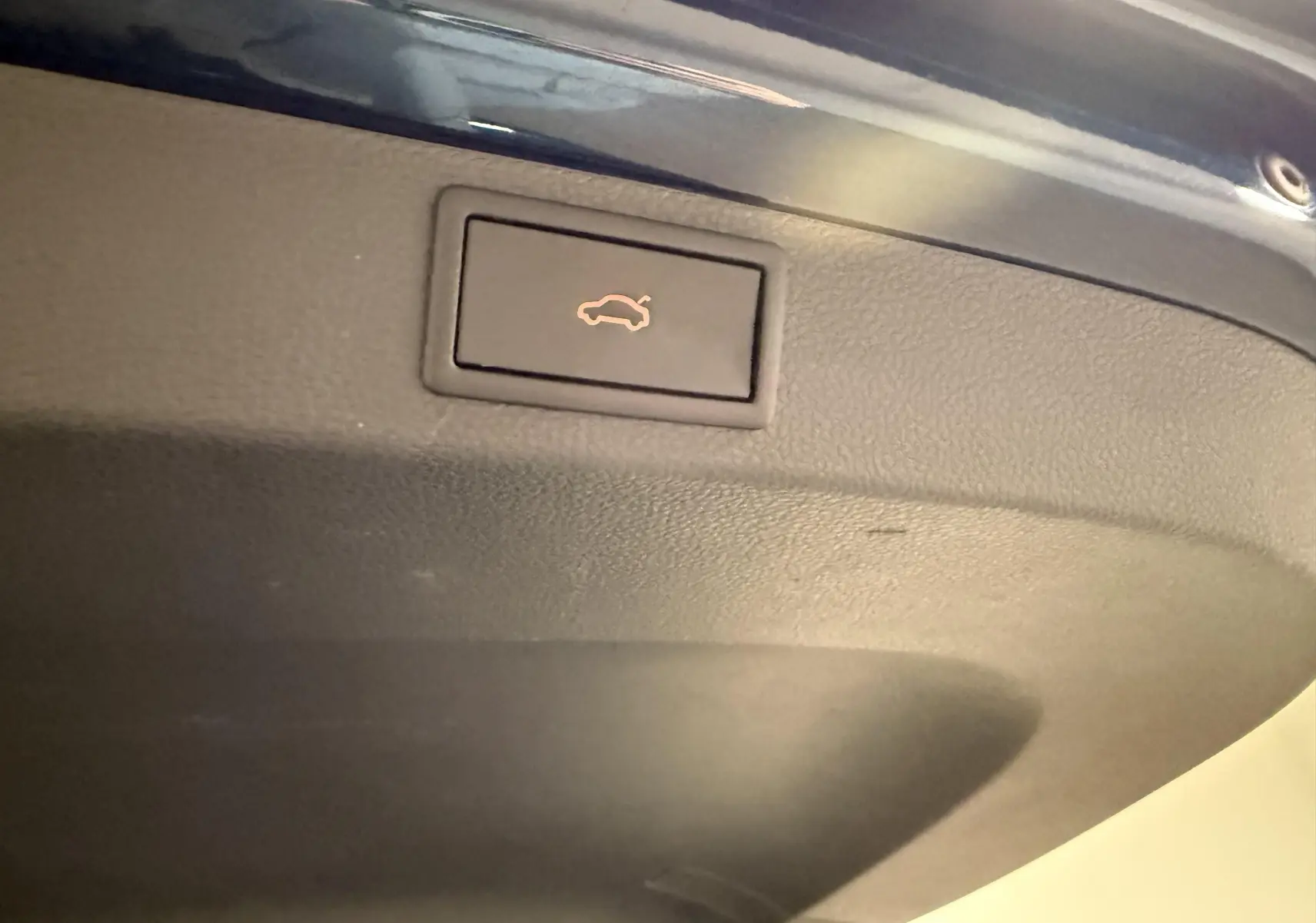 Bouton d'ouverture électrique du coffre sur le bord intérieur d'un Skoda Karoq bleu lave, vue rapprochée.