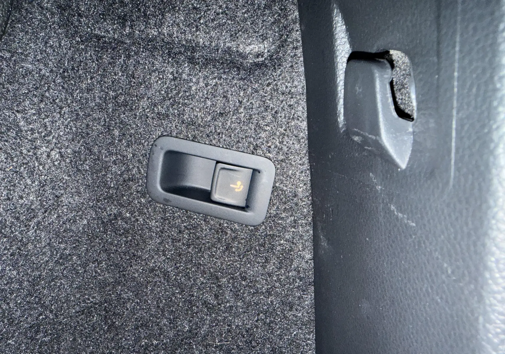 Gros plan sur le bouton de rabattement des sièges dans le coffre du Skoda Karoq 2023 bleu lave.