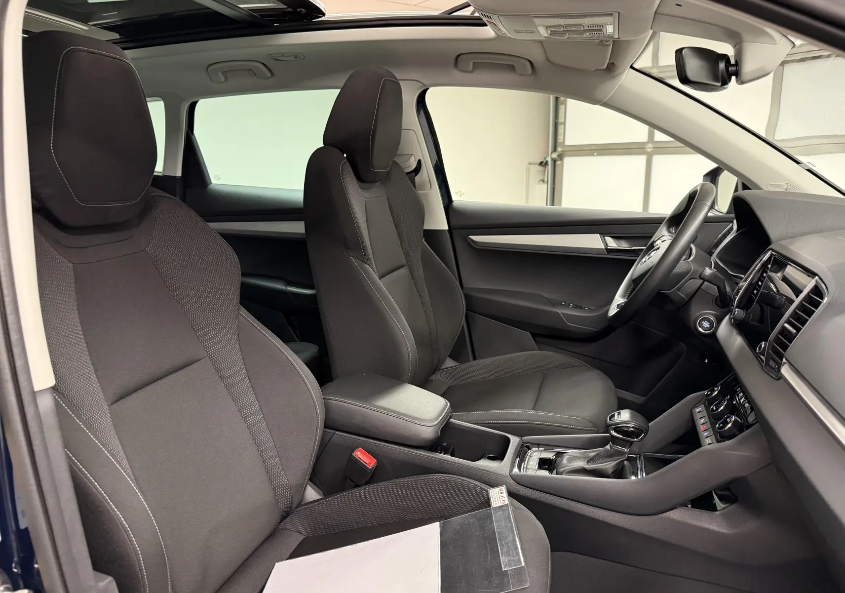 Vue intérieure côté conducteur du Skoda Karoq 2023 avec sièges noirs et toit ouvrant visible.