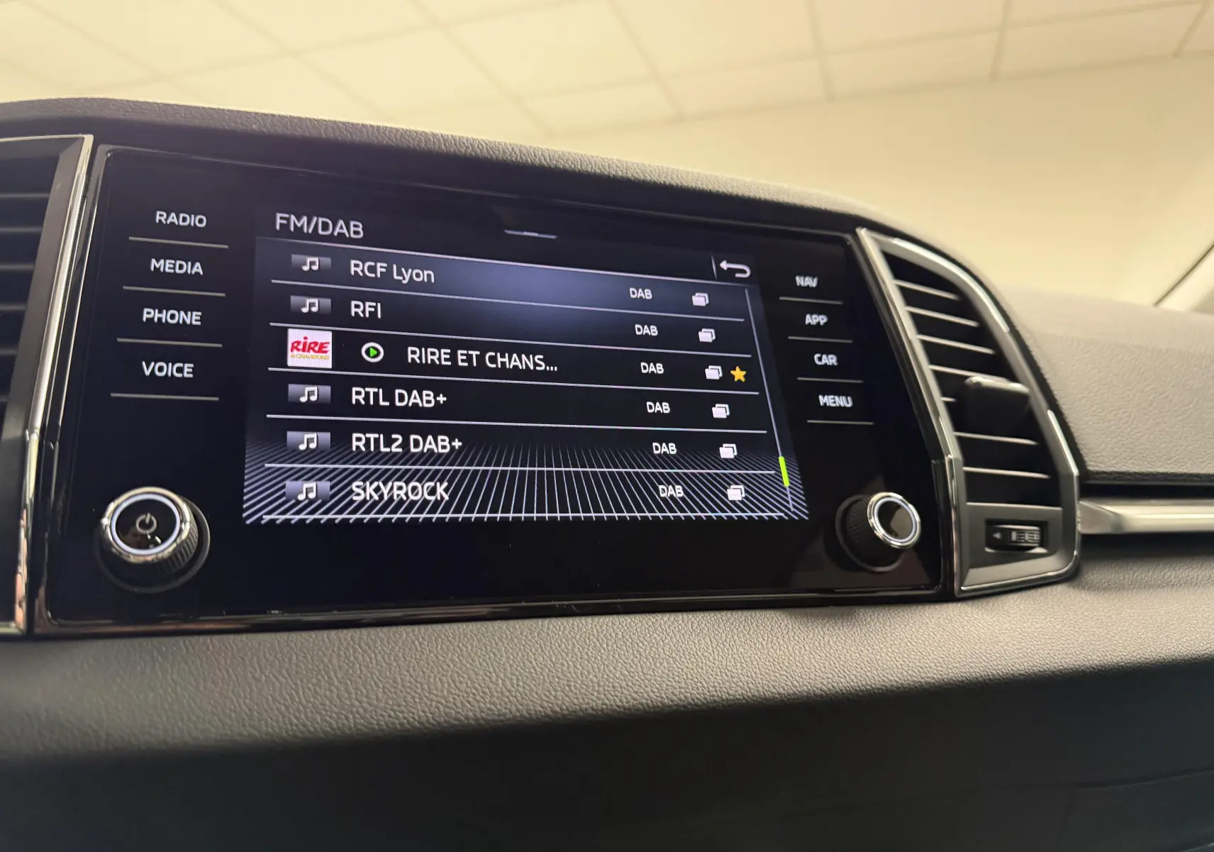 Écran tactile central du Skoda Karoq 2023 affichant les stations radio DAB, avec commandes autour et ventilation à droite.