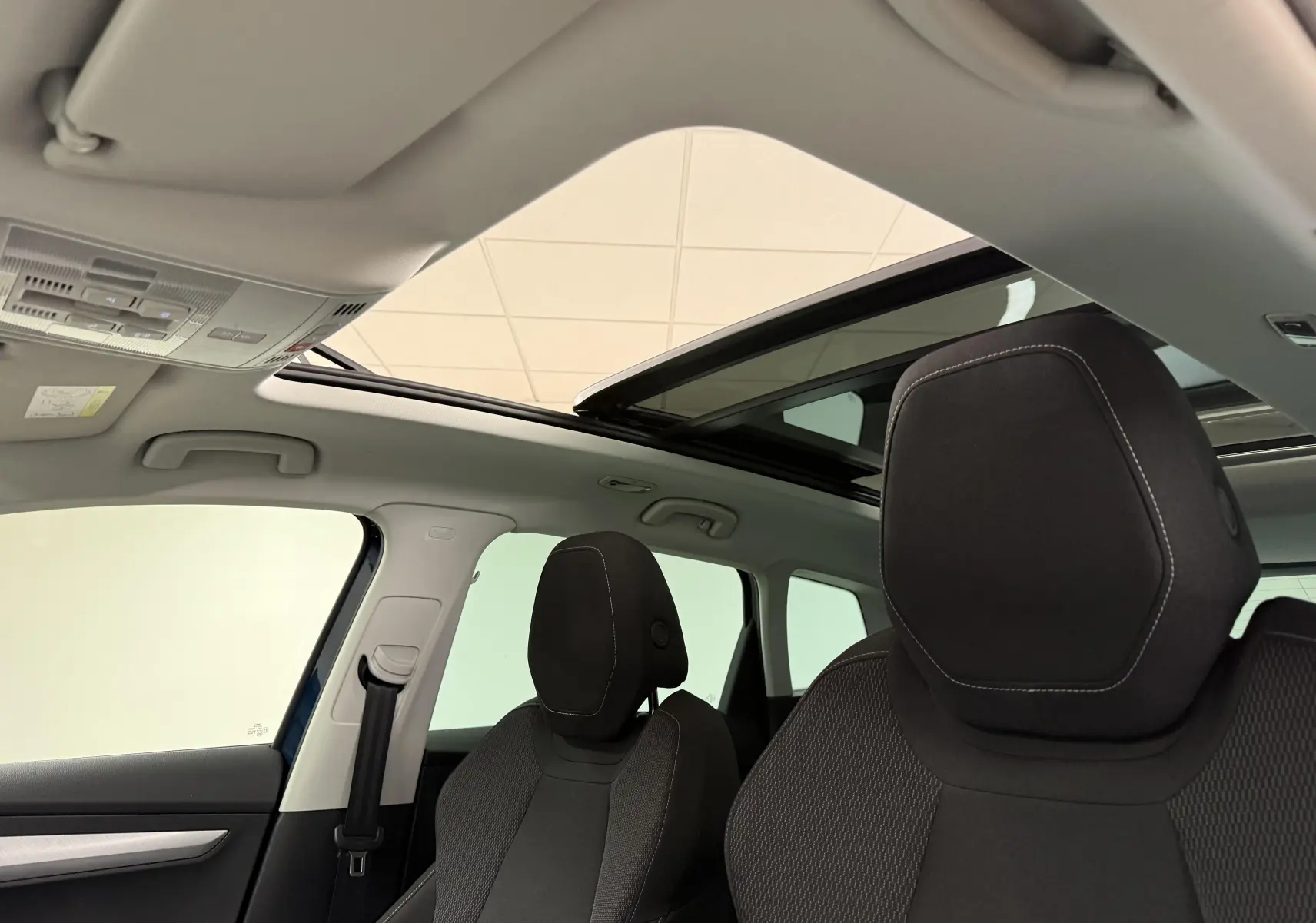 Vue intérieure du toit ouvrant panoramique et des sièges avant noirs du Skoda Karoq Bleu Lave 2023.