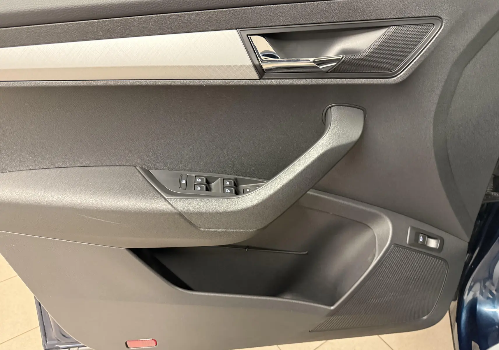 Gros plan sur la porte avant gauche du Skoda Karoq bleu lave, montrant les commandes de vitres et la poignée intérieure chromée.