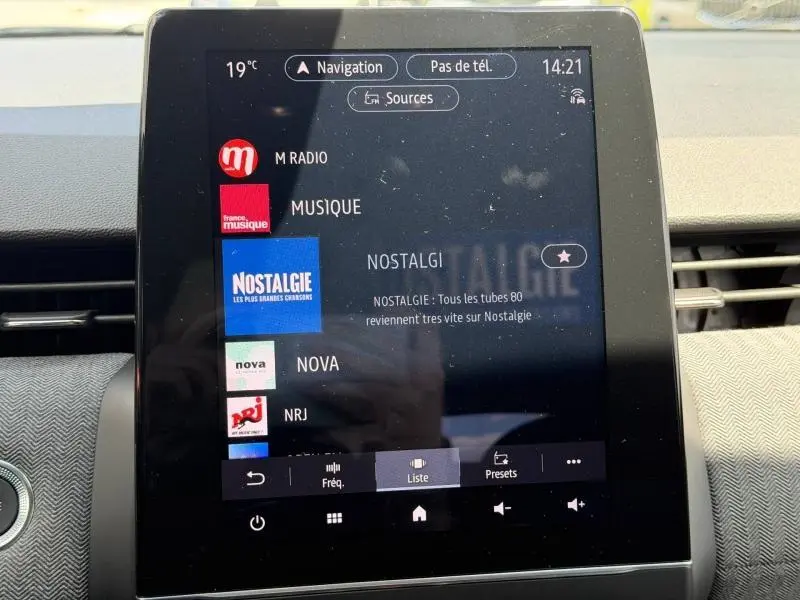 Écran tactile central de la Renault Clio 1.6 E-Tech rouge Flamme, affichant la liste des stations radio en intérieur.