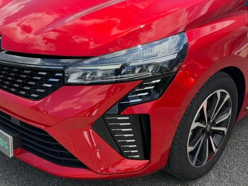Gros plan sur l'avant droit de la Renault Clio 1.6 E-Tech 145ch hybride Rouge Flamme, mettant en valeur le phare et la calandre.