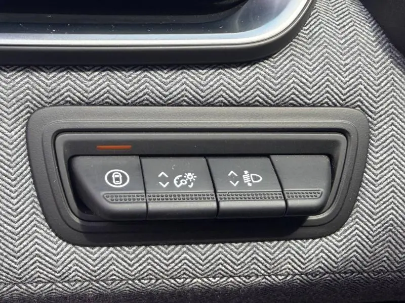 Gros plan sur les commandes de réglage des phares et du tableau de bord de la Renault Clio 1.6 E-Tech rouge Flamme 2025.