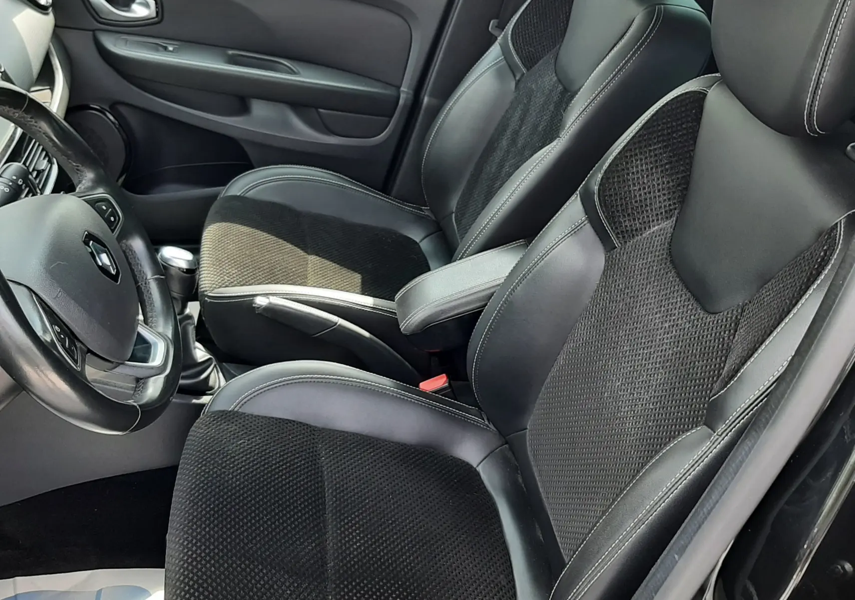 Vue intérieure côté gauche de la Renault Clio IV noire, mettant en valeur les sièges mixtes cuir et tissu avec surpiqûres blanches.