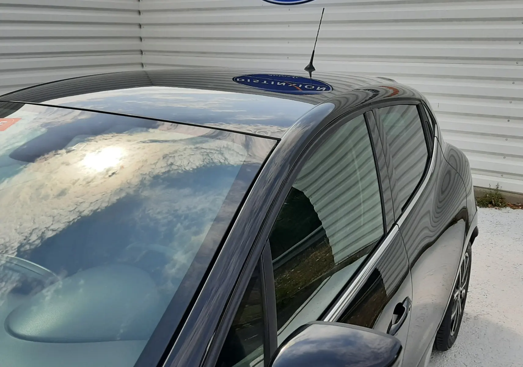Vue plongeante côté gauche sur Renault Clio IV noire 5 portes, avec rétroviseur et toit brillant reflet ciel.