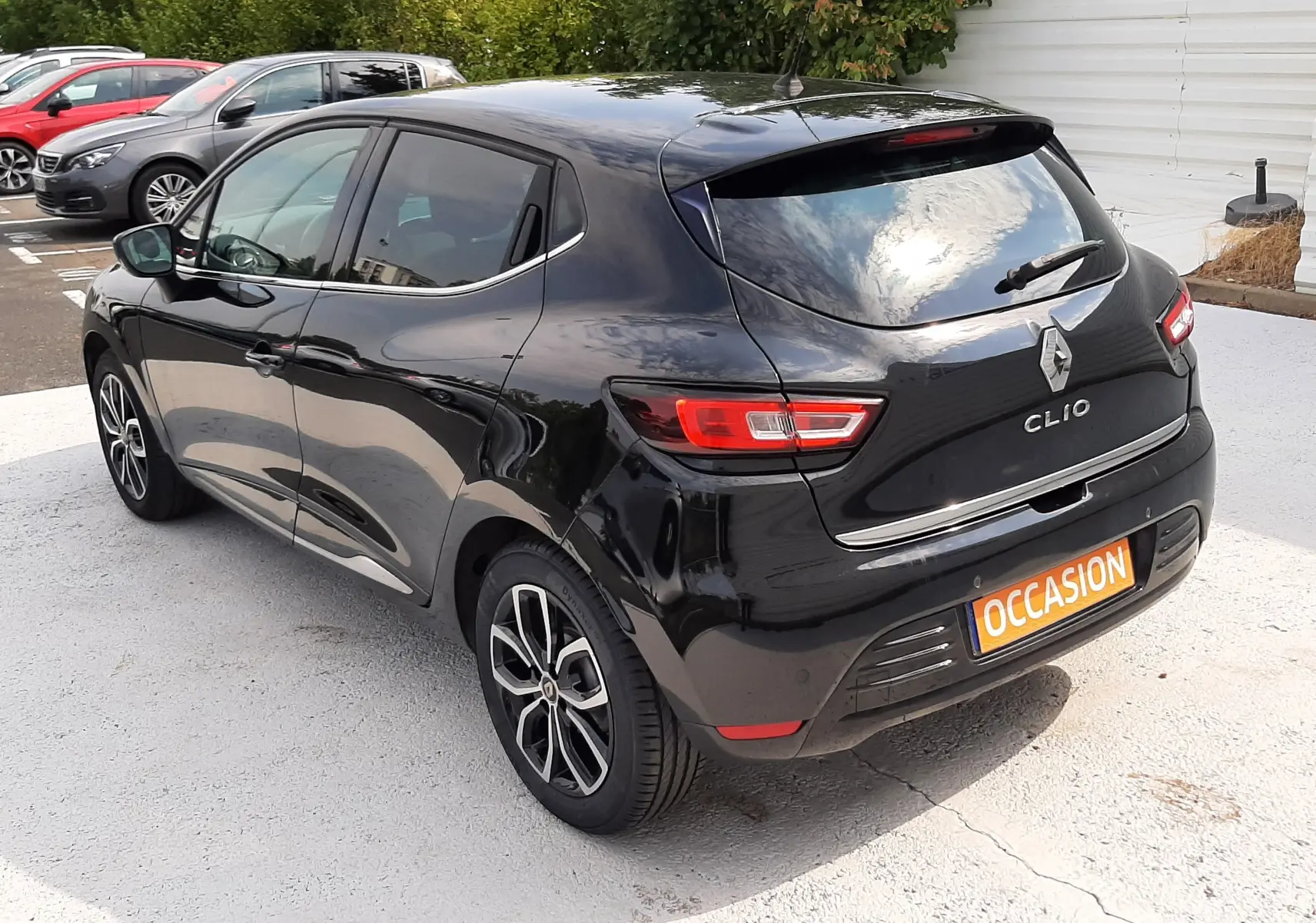 Vue 3/4 arrière droite d'une Renault Clio IV noire, avec jantes alliage et feux arrière LED, stationnée sur parking.