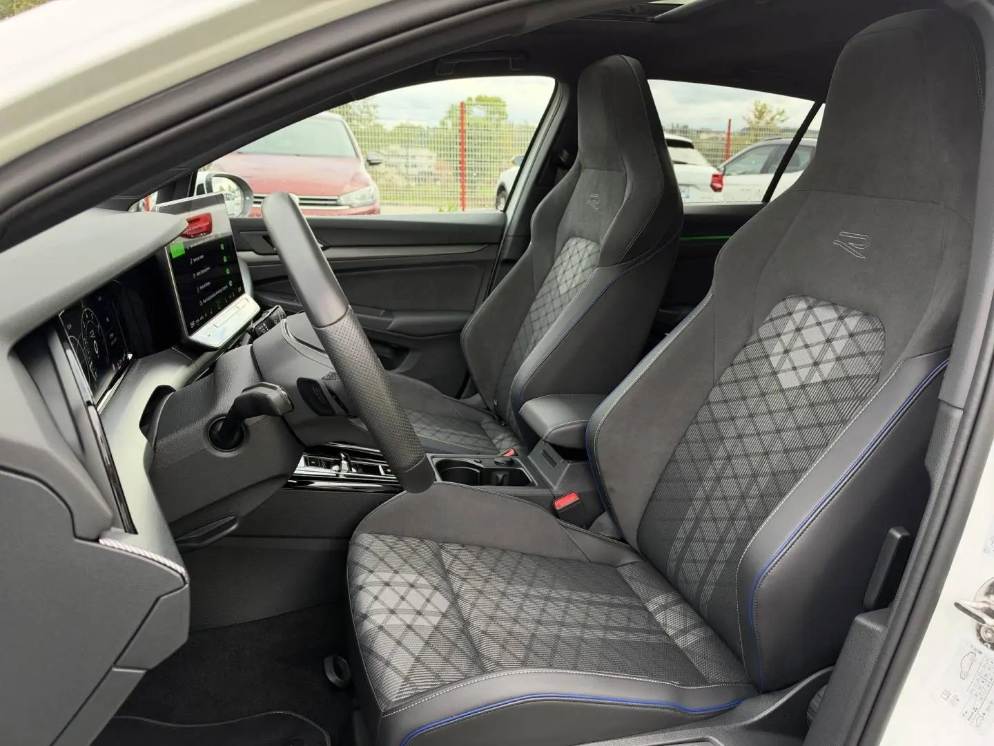 Vue intérieure côté conducteur de la Volkswagen Golf 1.5 eTSI R-Line 2025, sièges sport gris à surpiqûres bleues.