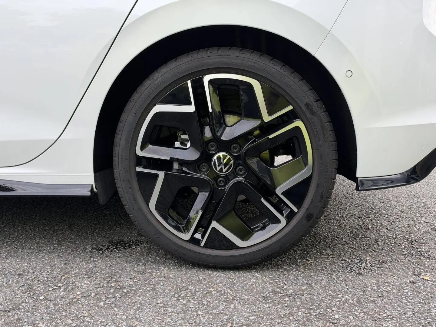 Gros plan sur la roue arrière droite d’une Volkswagen Golf blanche Oryx nacrée avec jante alu noire et argentée R-Line.