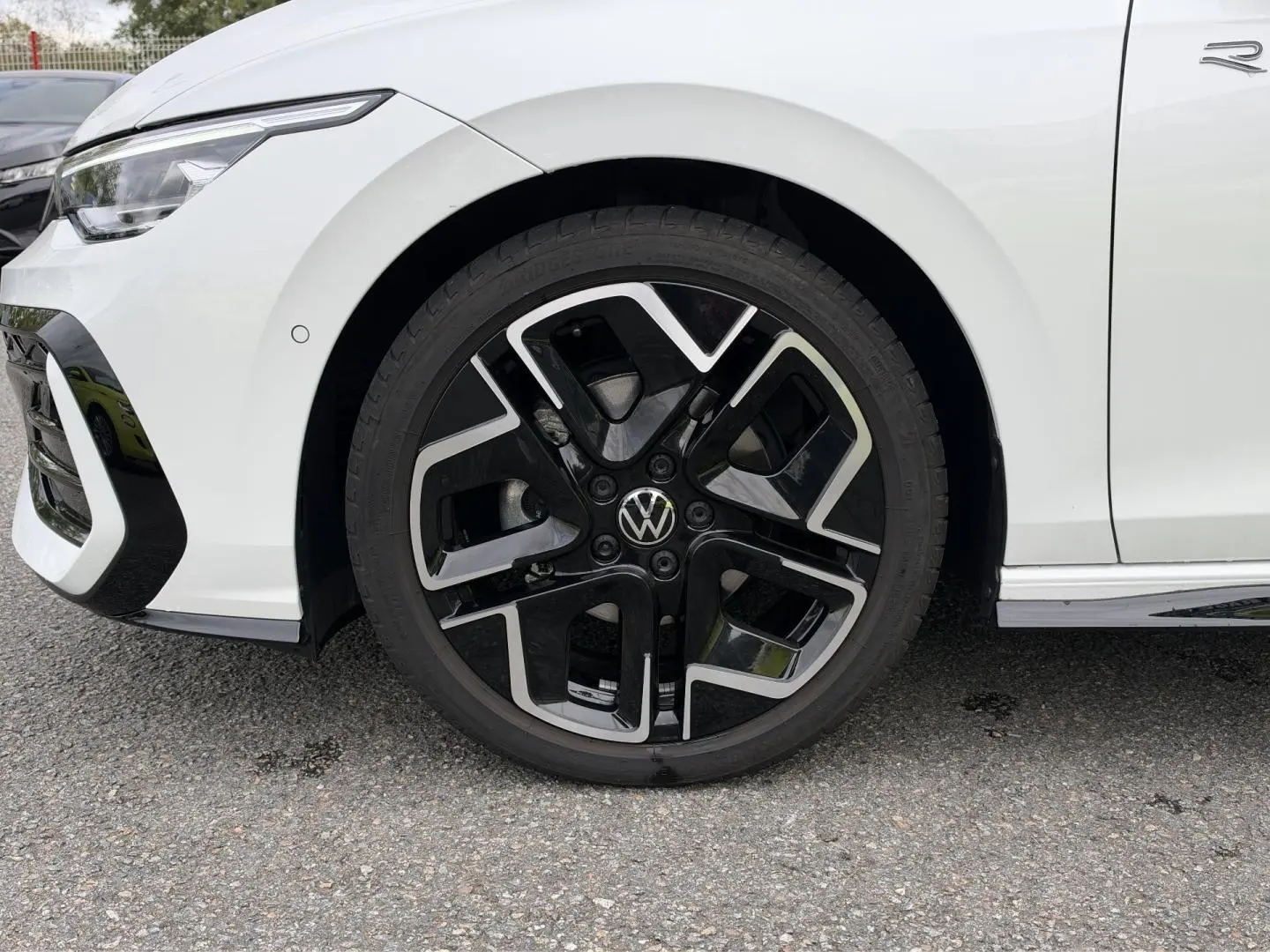 Gros plan sur la roue avant gauche de la Volkswagen Golf blanche Oryx nacrée avec jante alu noire et argentée R-Line.