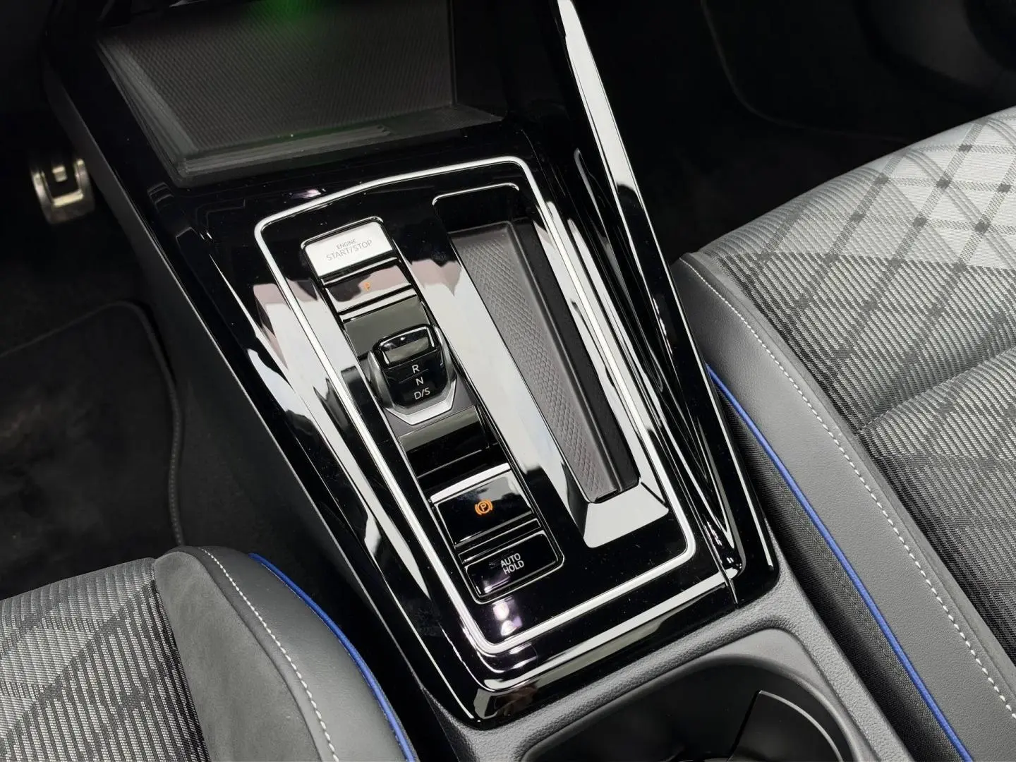 Vue plongeante sur la console centrale brillante avec levier de vitesses électronique et siège tissu gris à surpiqûres bleues de la Volkswagen Golf.