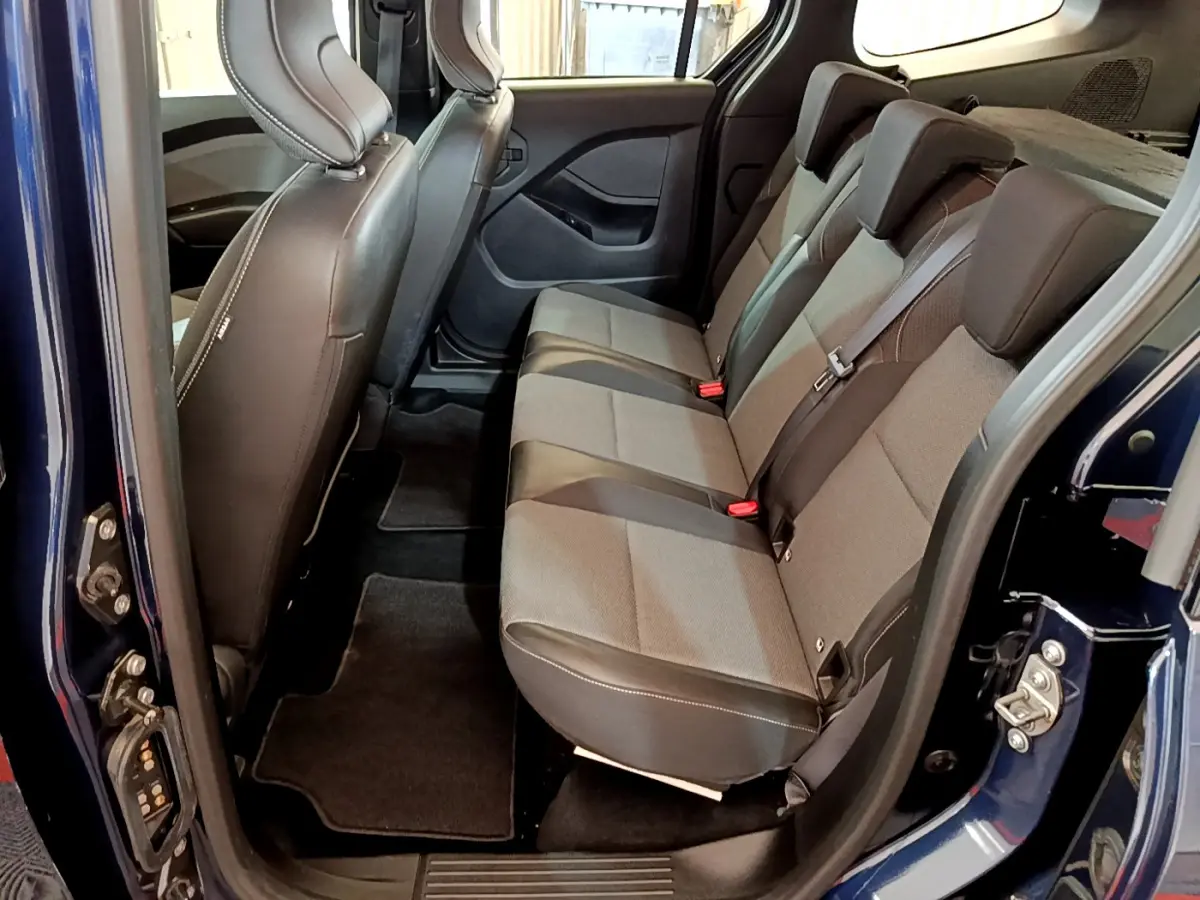 Vue latérale intérieure côté droit du Renault Kangoo bleu 2023, sièges arrière en tissu gris et noir avec ceintures de sécurité.