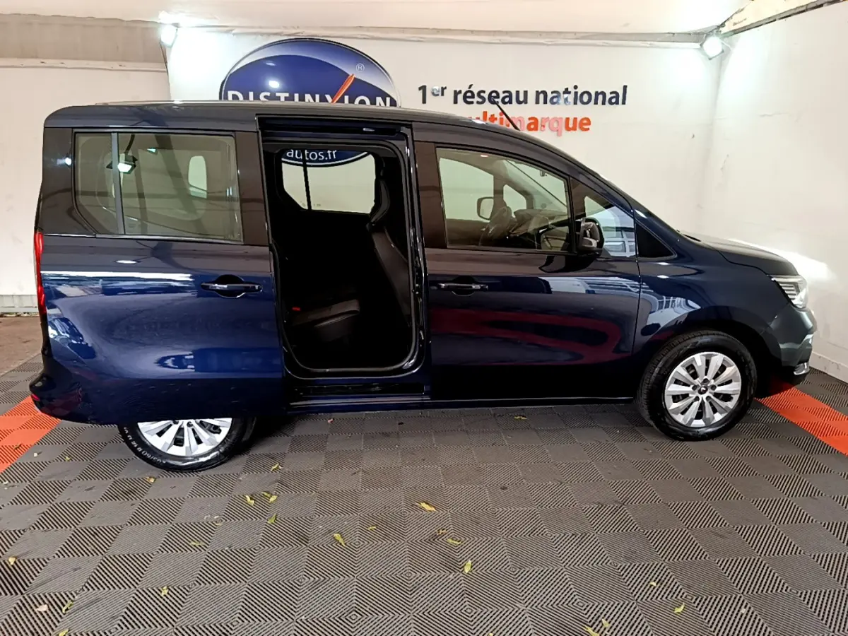 Profil droit d’un Renault Kangoo bleu 2023 avec porte coulissante arrière ouverte, stationné en intérieur.